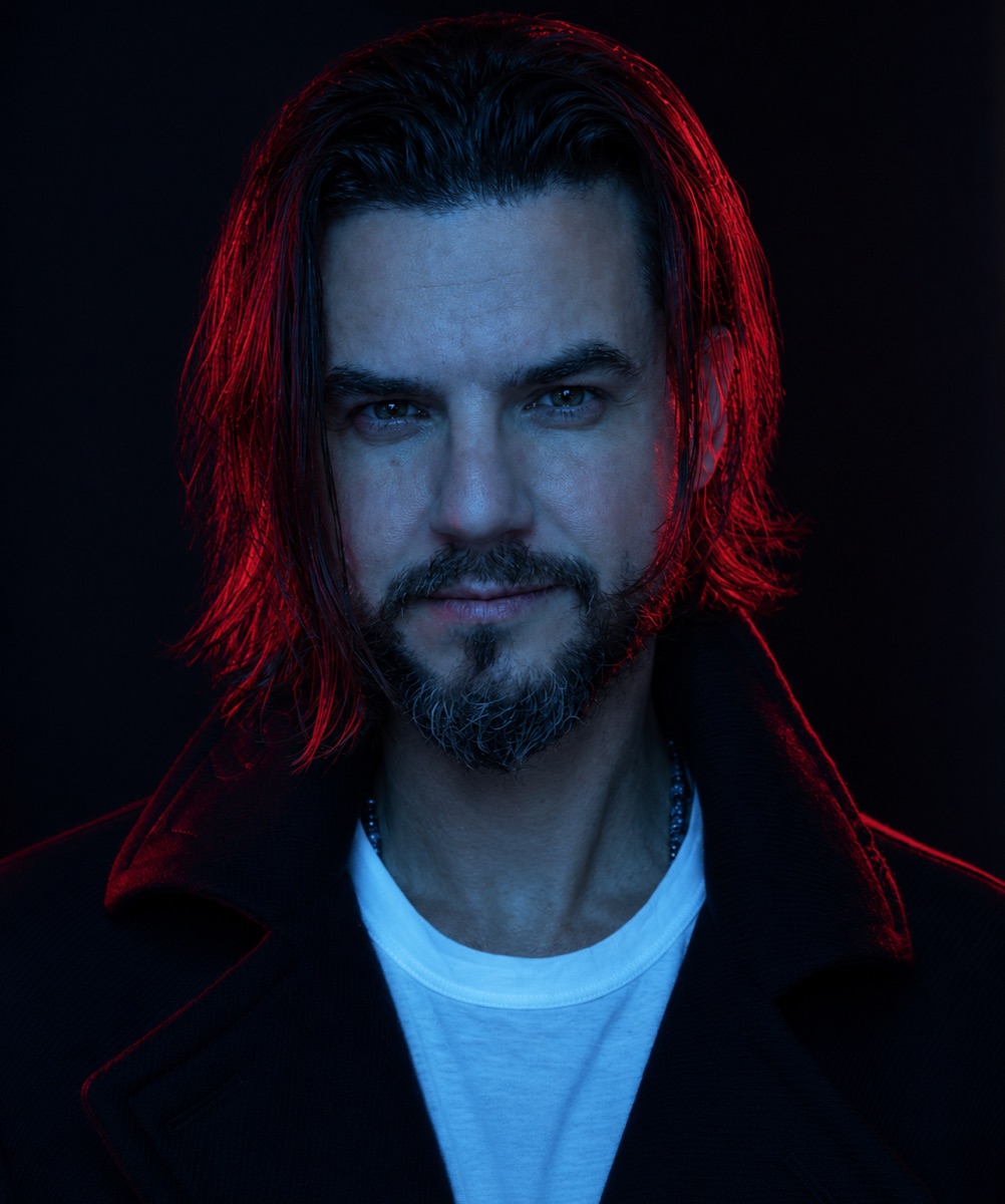 Portrait of Ric Neves, lit in red and blue against a black background
